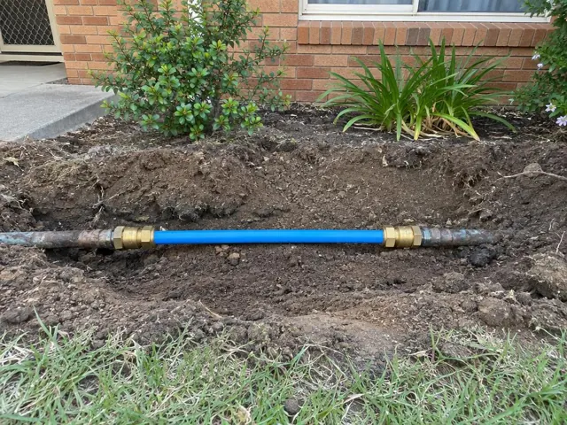 Exposed repaired water pipe in a garden trench beside a brick house in Gymea Bay