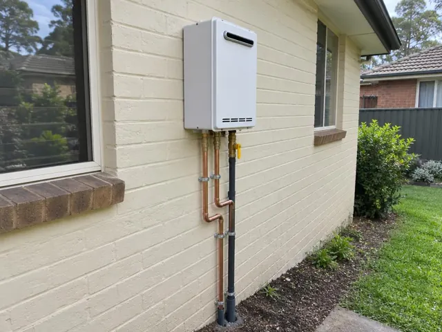 Wall-mounted hot water unit with copper and gas pipework on a painted brick house exterior in Miranda
