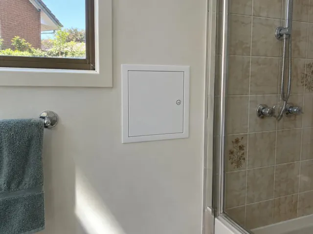Bathroom wall with a small access panel beside a tiled shower and window in Miranda